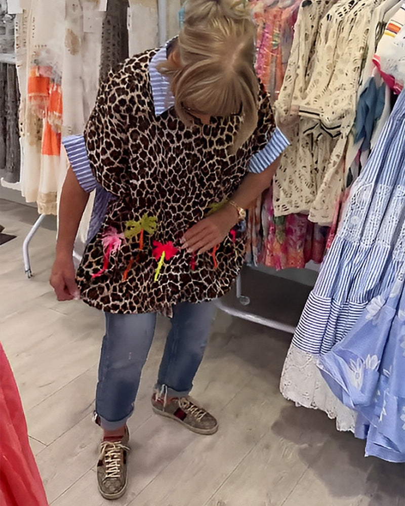 Dame med vidt skårne poncho-tunika med leopardprint og dekorative flamingo-applikationer Skovae。